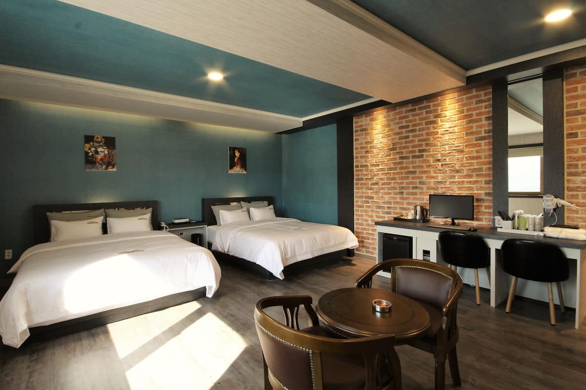 A hotel room with two beds, a desk with a computer, and a dining area with chairs.