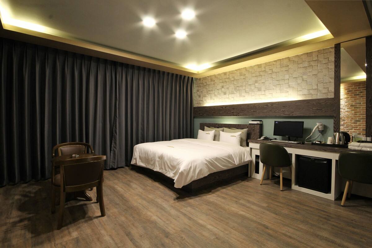 A hotel room with a bed, desk, chair, and curtains.
