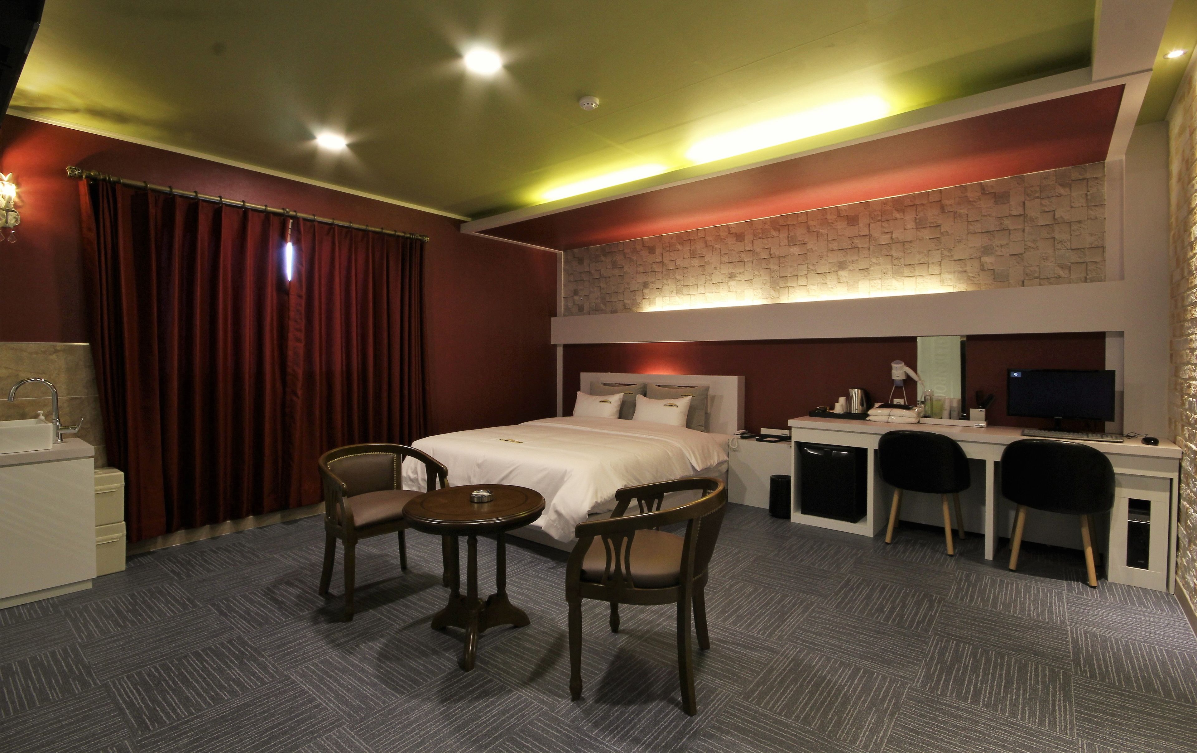 Habitación de hotel con cama, escritorio, dos sillas, una mesita y televisión.