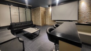 Una sala de conferencias moderna con un sofá de cuero negro, una mesa con cubierta de vidrio y una pizarra.
