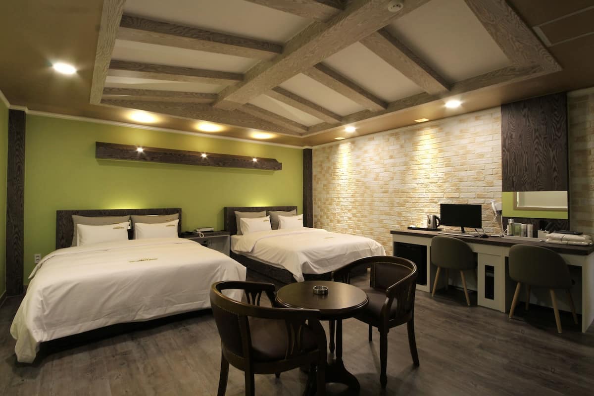 A hotel room with two beds, a desk, a computer, and a small table with chairs.
