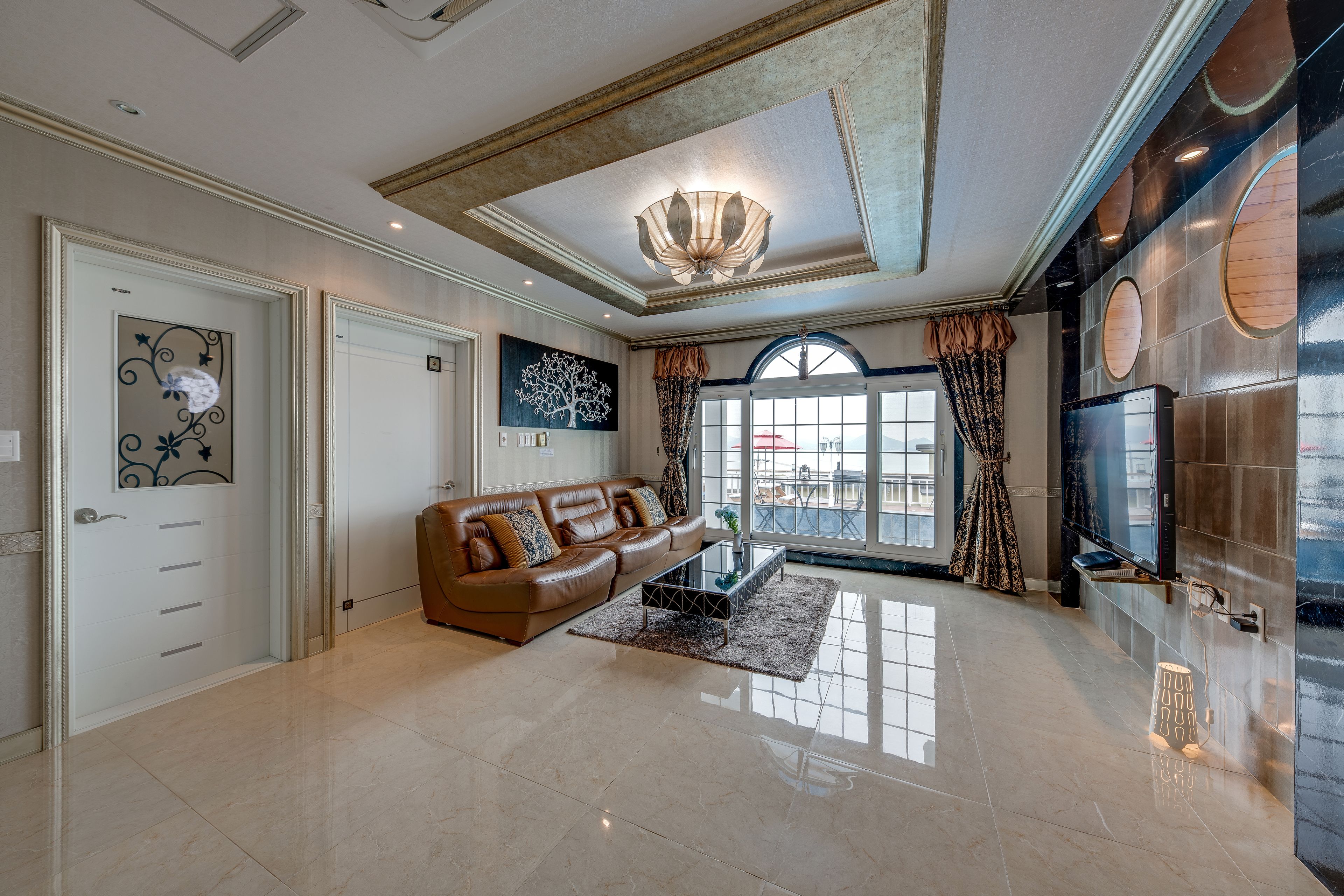 A spacious living room with a brown leather sofa, a coffee table, and a large window with curtains.