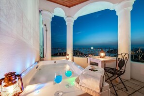 A balcony with a hot tub, two glasses of blue liquid, a wicker basket, a table with a candle, and a chair. - Alhambra Pension (Namhae)