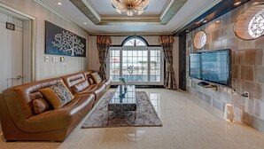 Un salon spacieux avec un canapé en cuir marron, une table basse en verre et un grand téléviseur à écran plat fixé au mur.