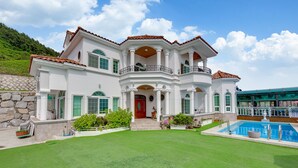Une grande maison blanche à deux étages, avec une porte rouge, un balcon et une piscine.