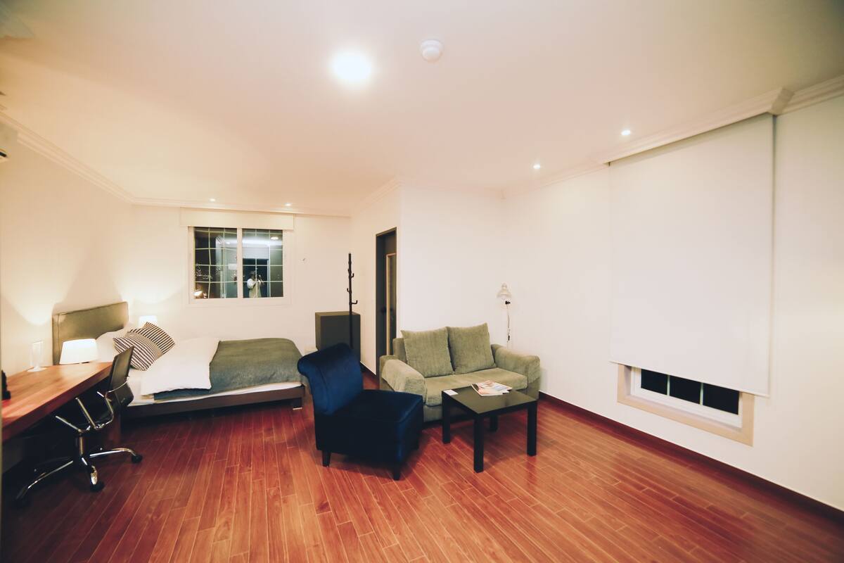 Una sala de estar moderna con suelo de madera, un sofá, un sillón, una mesa de centro y un escritorio con una lámpara.