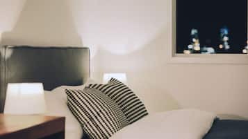 A neatly made bed with a striped pillow, a bedside lamp, and a view of city lights through a window.