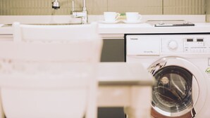 A front view of a washing machine with a control panel, a faucet, and two white cups on a counter. - GONGGAN Residence Hotel (Geoje)
