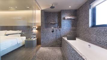 A modern bathroom with a glass shower enclosure, a separate shower area, a large bathtub, and a built-in shelf with toiletries.