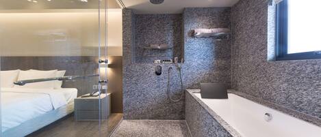 Un baño moderno con cabina de ducha de vidrio, zona de ducha separada, bañera grande y estante empotrado con artículos de aseo.