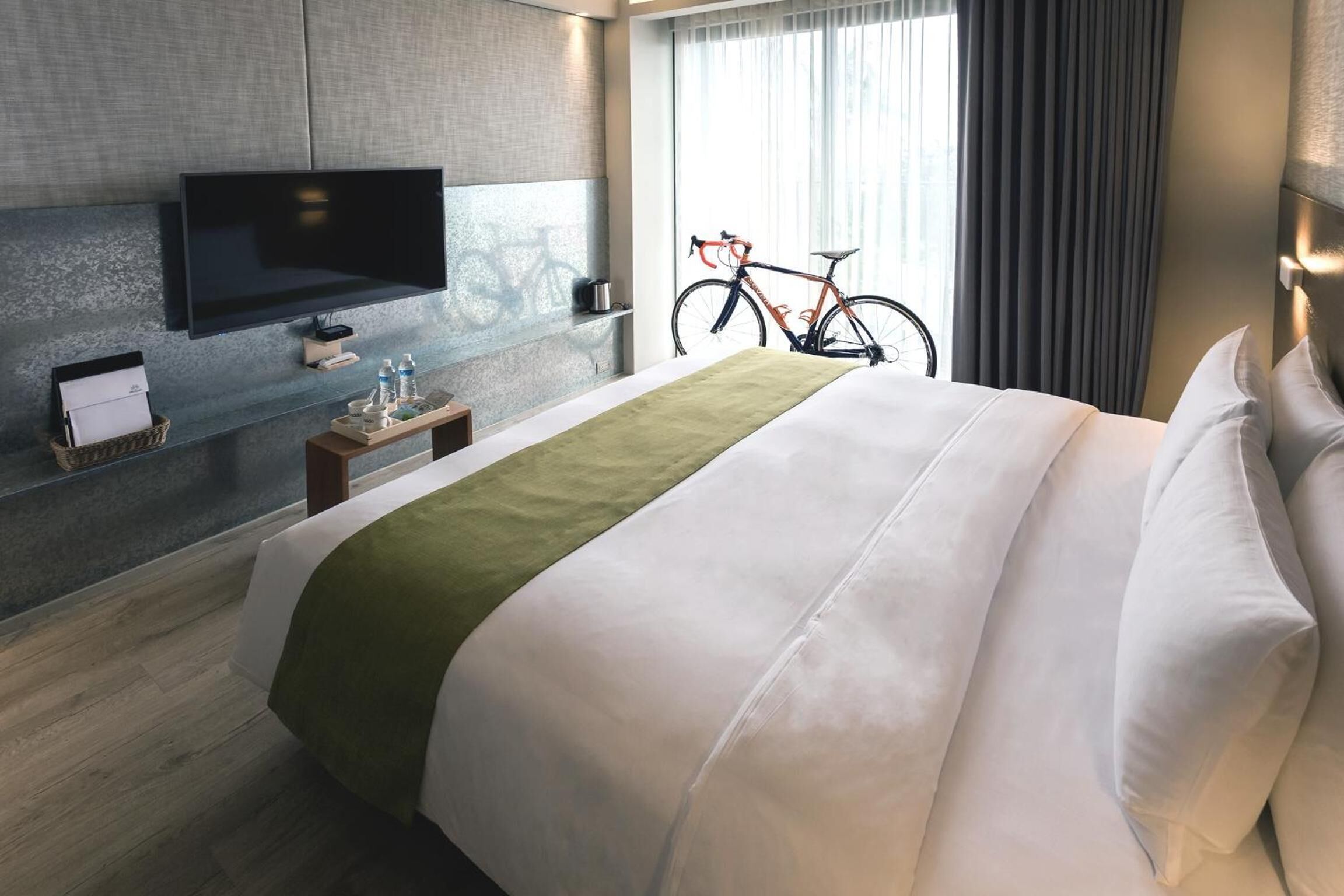 A hotel room with a bed, a television, a bicycle, and a window with curtains.