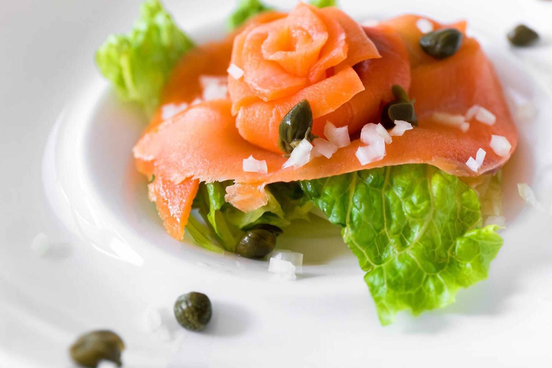 A dish with smoked salmon, capers, and diced onions on a bed of lettuce.