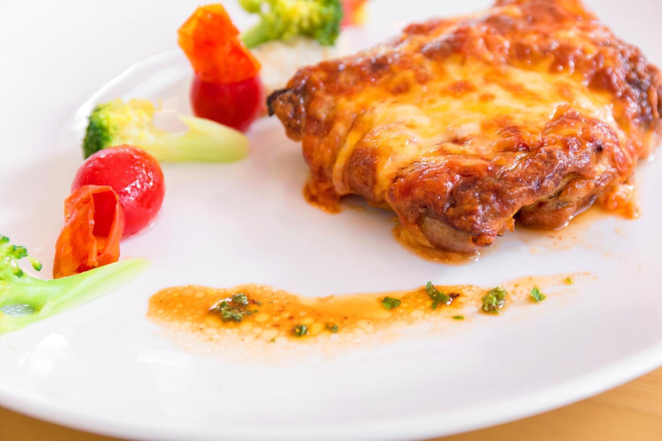 Un plato con un trozo de pollo bañado en queso y salsa, acompañado de verduras.