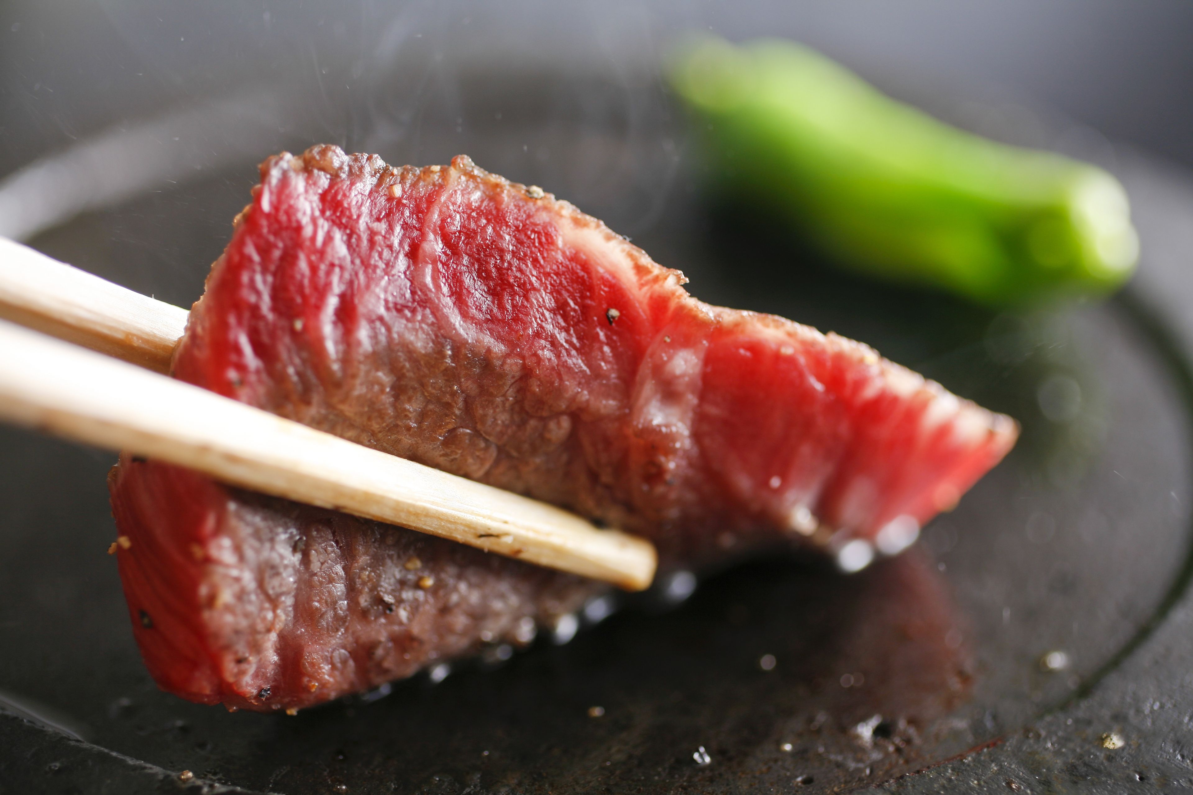 A piece of meat on a plate with chopsticks.