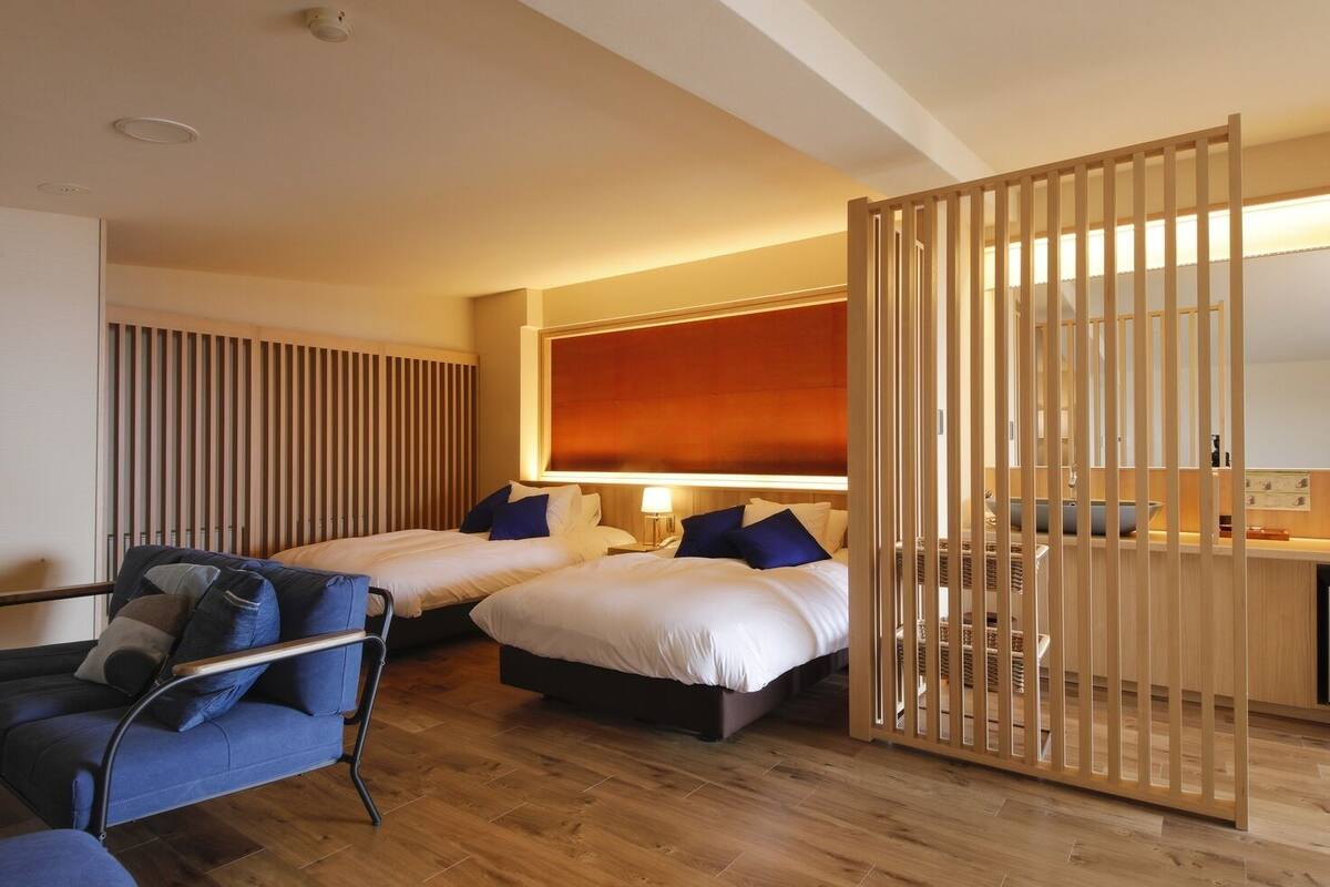 Ein Hotelzimmer mit zwei Betten, einem Sessel, einem Schreibtisch und einem großen Fenster.