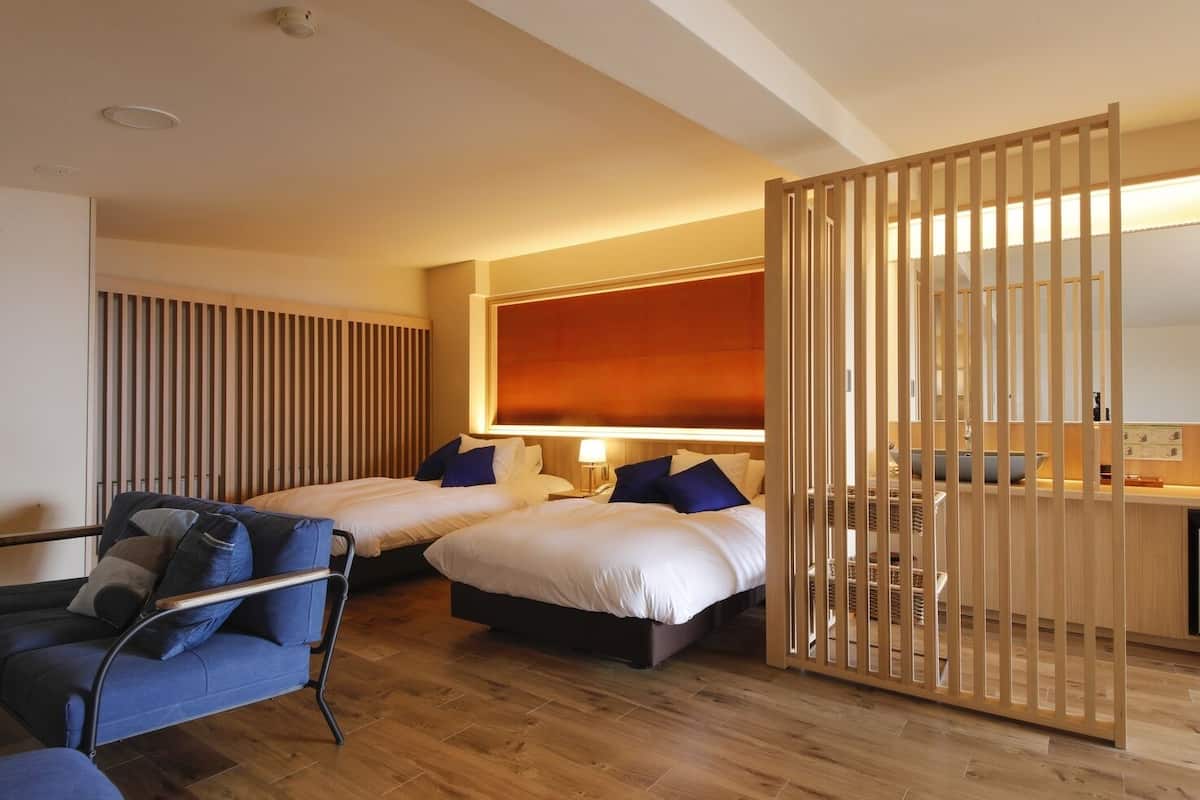 Habitación de hotel con dos camas, una silla, un escritorio y un ventanal grande.