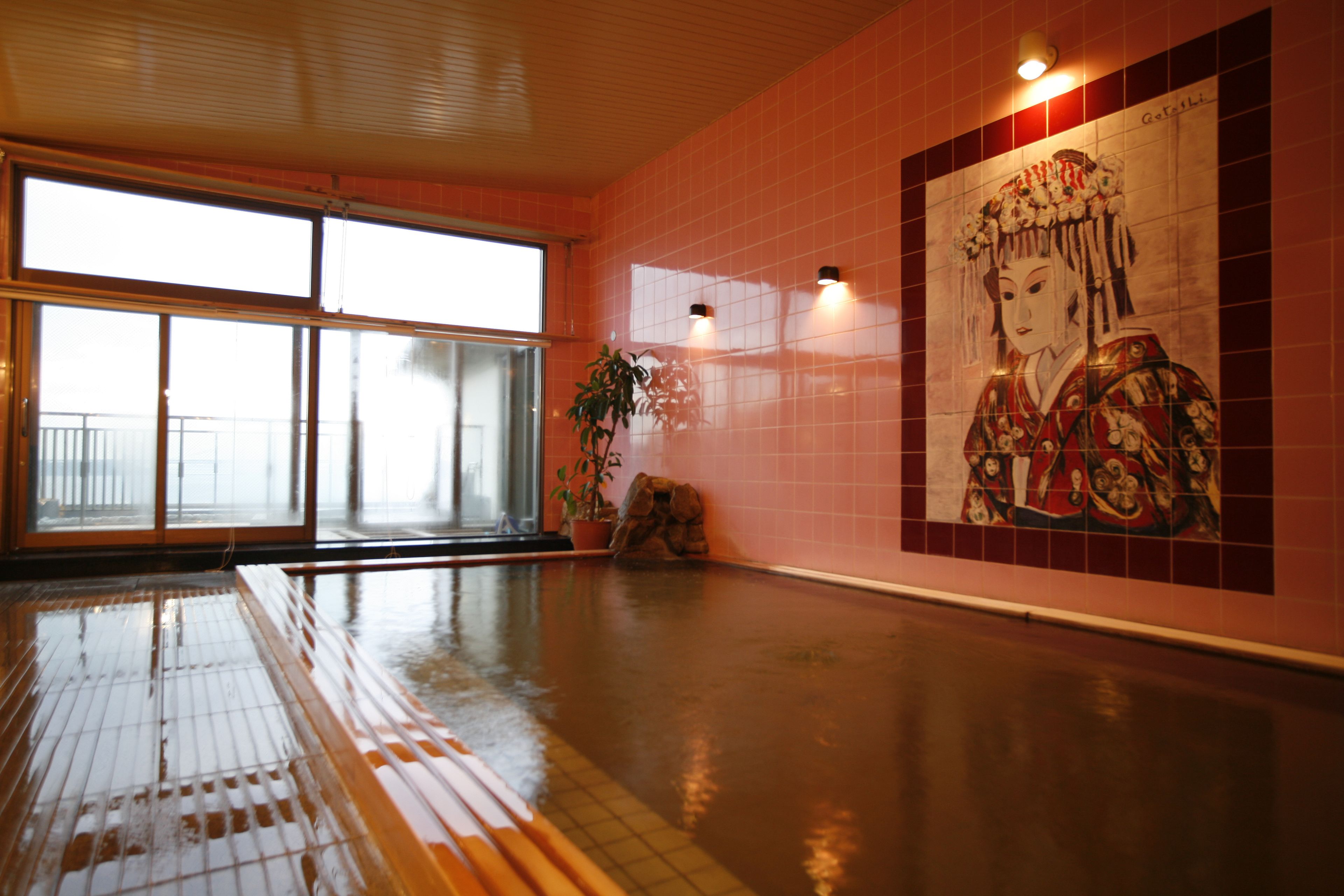 A spacious indoor area with a large window, a tiled wall with a mural, and a wet floor indicating recent cleaning or maintenance.