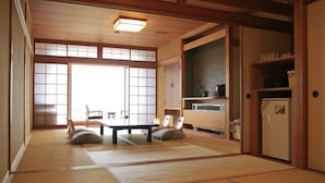 Een traditionele Japanse kamer met tatami vloerbedekking, schuifdeuren, een lage tafel met kussens en een koelkast.
