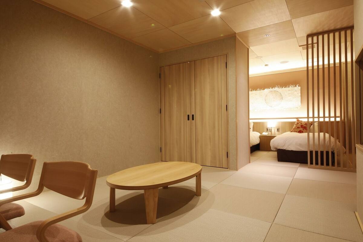 Ein Hotelzimmer mit Bett, Holztisch, Stühlen, Kleiderschrank und einer Raumtrennung.