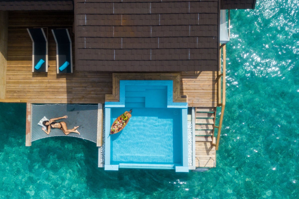 An aerial view of a wooden overwater villa with a swimming pool, a deck, and a boat.