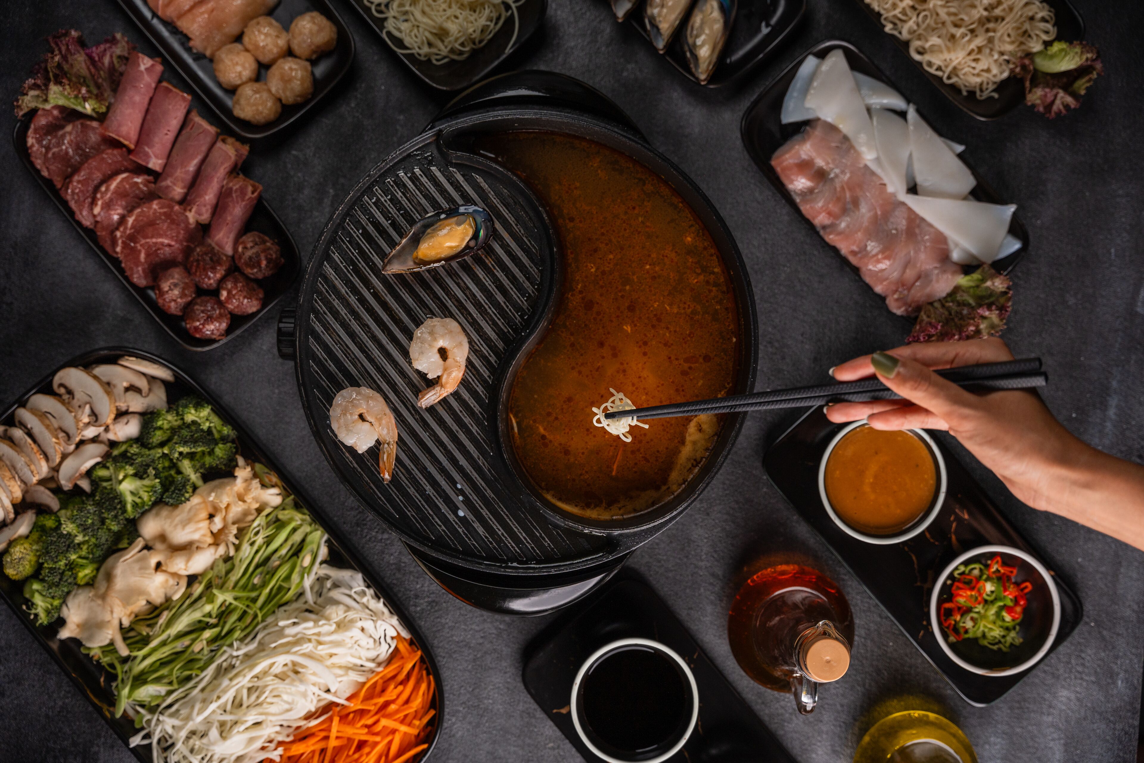 A variety of food items including meats, vegetables, and seafood arranged around a central hot pot.