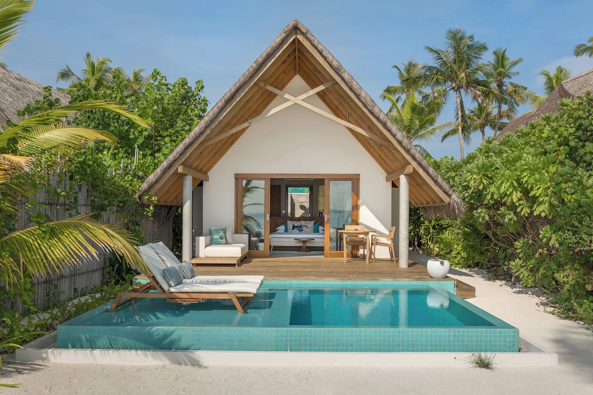 A beachfront villa with a pool, wooden deck, and a thatched roof.