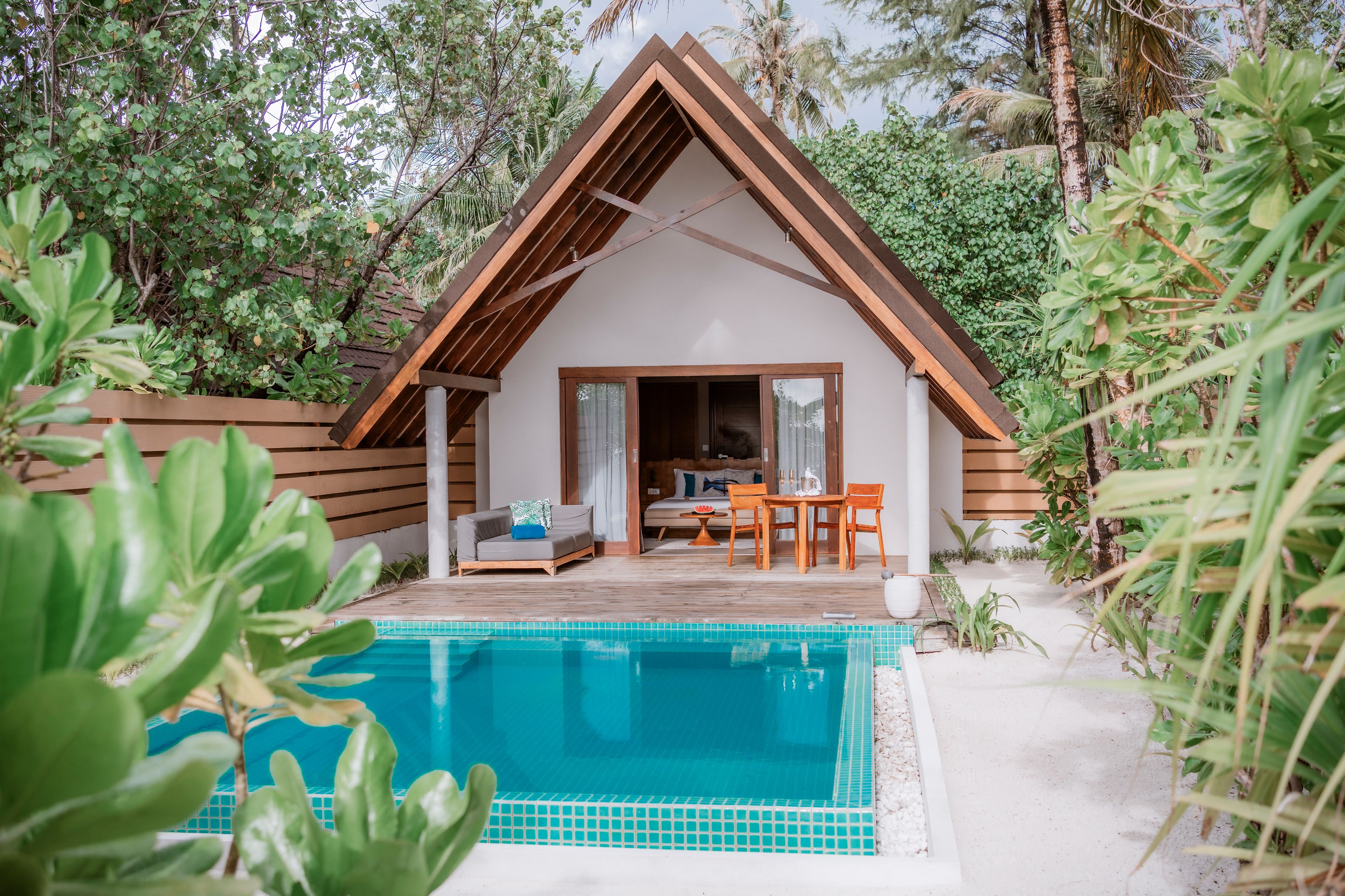 A modern villa with a pool, wooden deck, and a dining area.