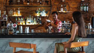 A bar with wooden shelves and a marble countertop, two wooden barstools, and a person preparing a drink.