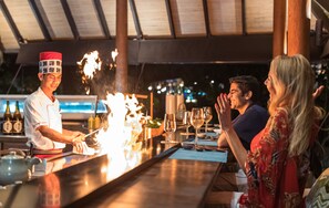A chef performing a fire trick at a bar with a pool view in the background. - Fushifaru Maldives (Fushifaru)