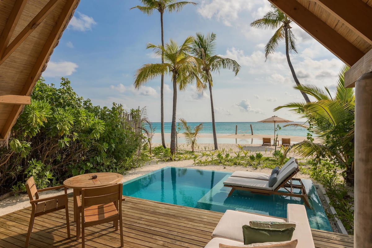 A wooden deck with a pool, lounge chairs, and a table.