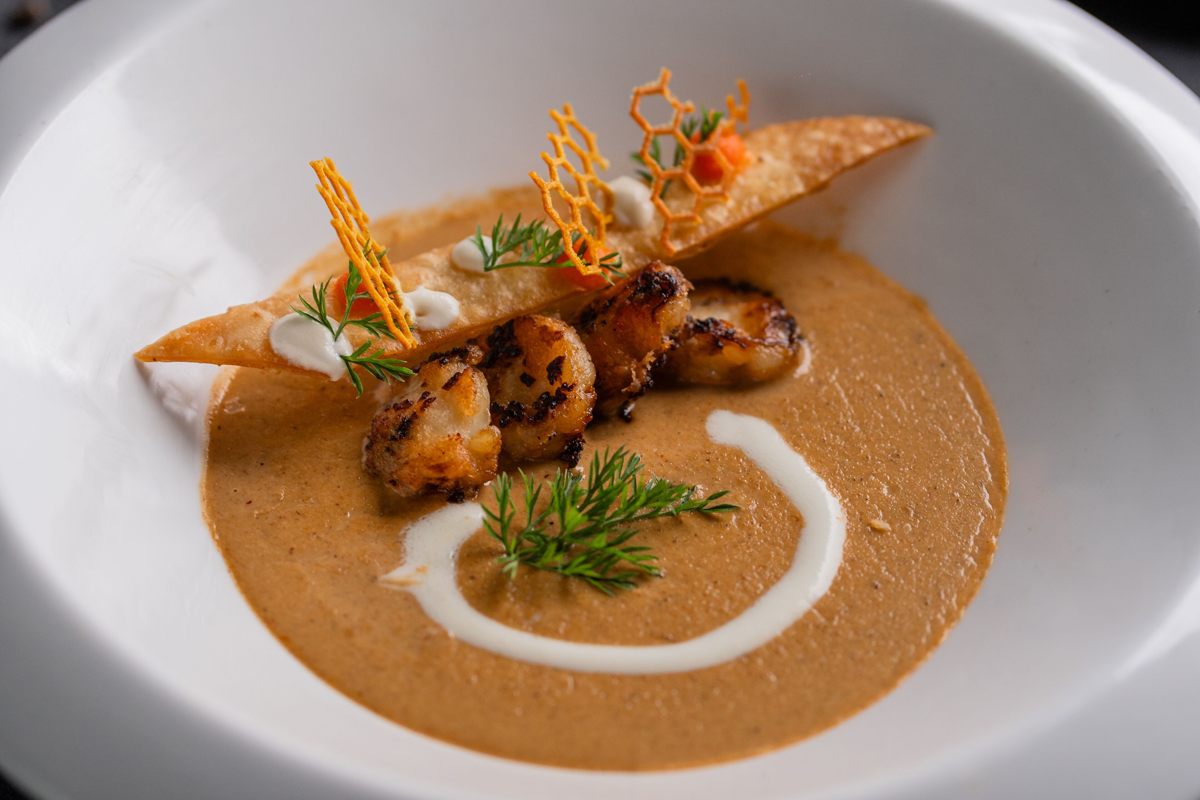 A white plate with a creamy soup, grilled meat, and garnishes.