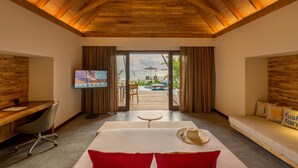 A room with a wooden ceiling, a bed, a desk, a TV, and a view of an outdoor pool and beach. - Fushifaru Maldives (Fushifaru)
