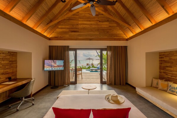 A room with a wooden ceiling, a bed, a desk, a TV, and a view of an outdoor pool and beach. - Fushifaru Maldives (Fushifaru)