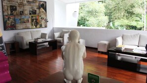 A living room with a large window, a white sofa, a coffee table, and a statue of a child. - VillaTel Salse (Bandung)