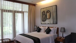 A hotel room with a large bed, a nightstand, a chair, and a painting on the wall. - VillaTel Salse (Bandung)