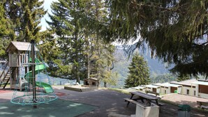 Un camping con mesas de picnic, un área de juegos con tobogán y cabañas con vista al lago.
