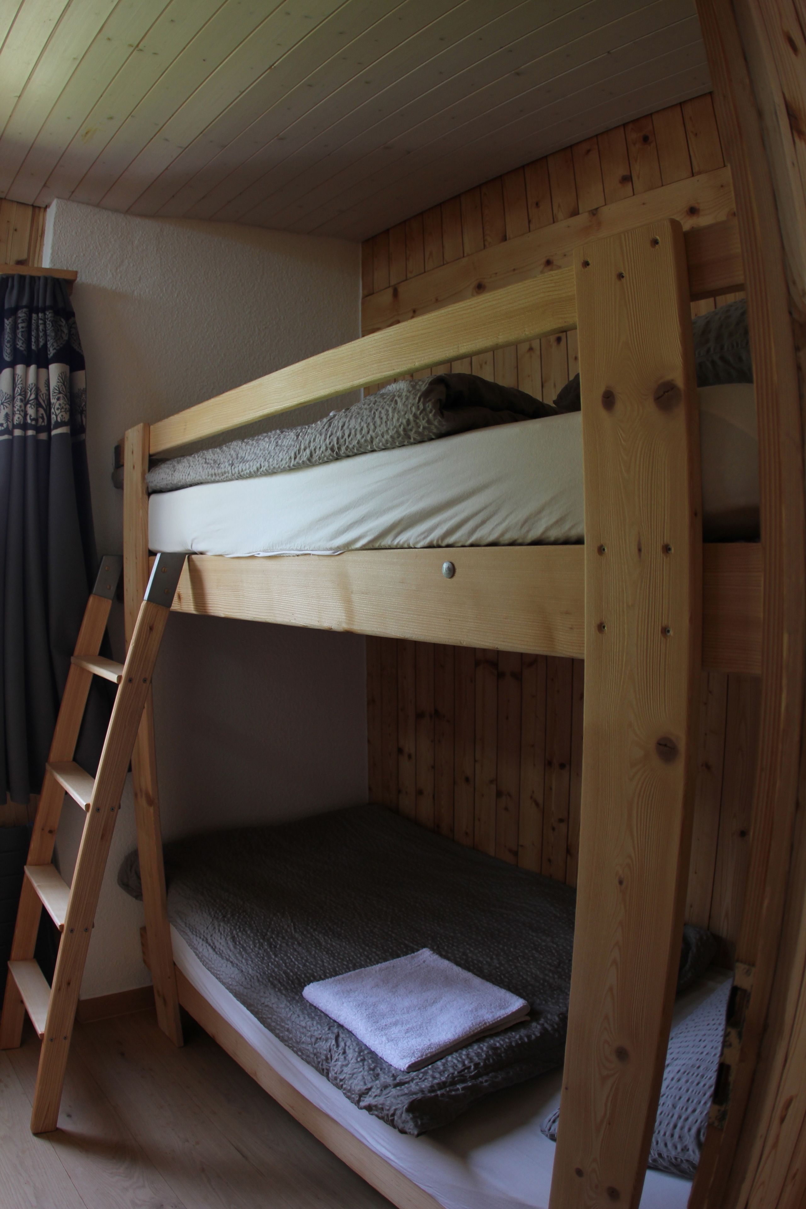 A bunk bed with a ladder, wooden walls, and a curtain.