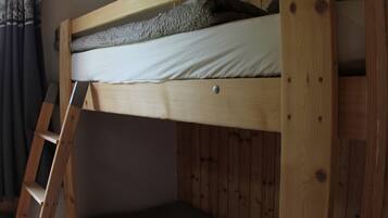 A bunk bed with a ladder, wooden walls, and a curtain.