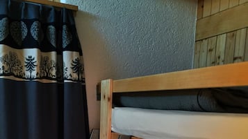 A bunk bed with a wooden ladder, a window with curtains, and a wooden wall.