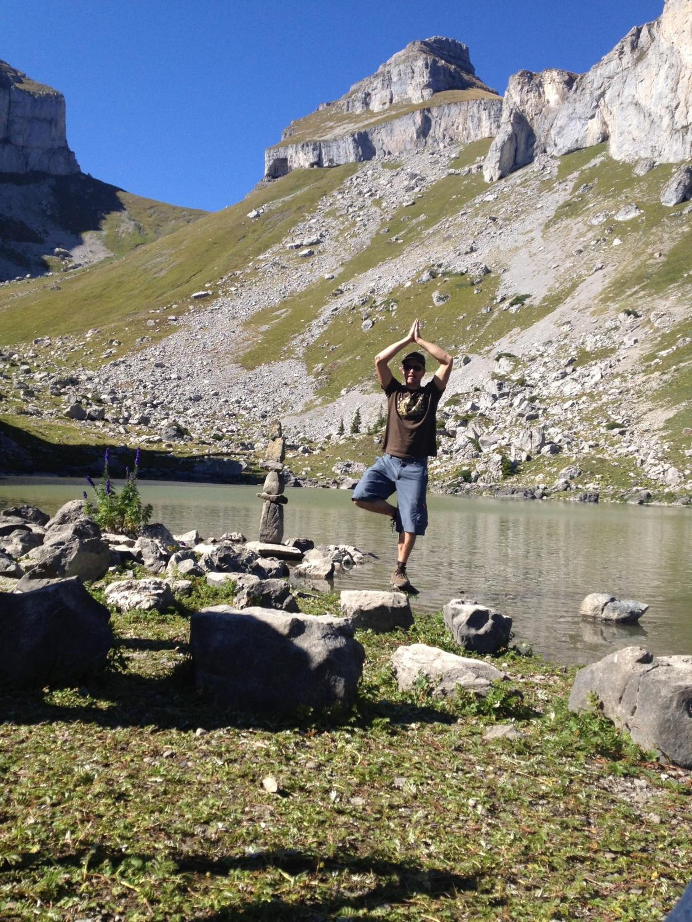 A person standing on rocks by a lake with mountains in the background.