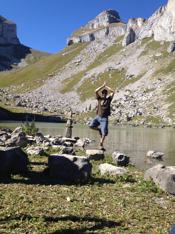 A person standing on rocks by a lake with mountains in the background. - Leysin Lodge (Leysin)