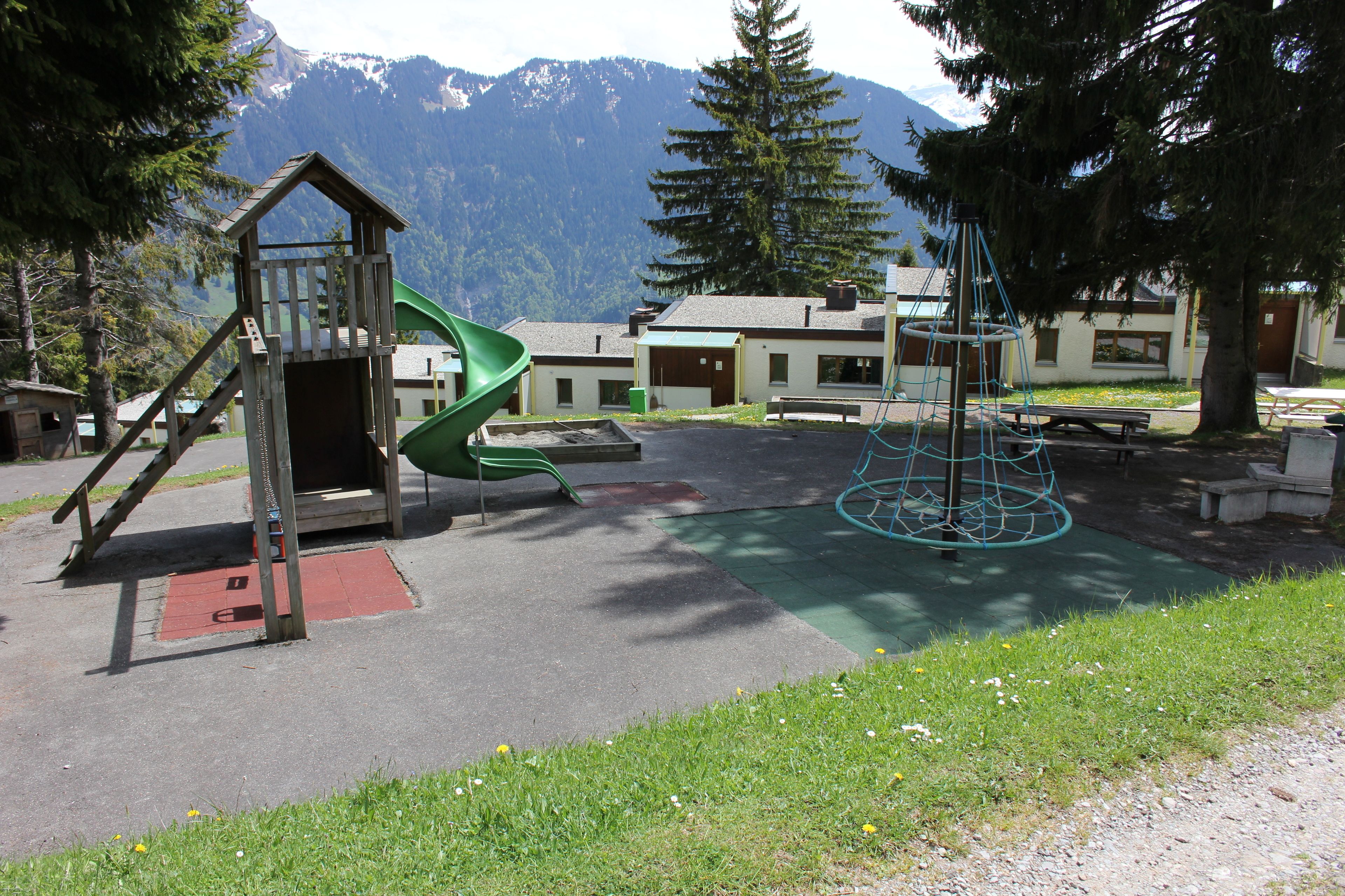 Un’area giochi con uno scivolo e una struttura per arrampicata, altalene e un’altalena sospesa con una corda.