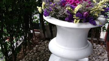 Um vaso pedestal branco com uma variedade de flores, cercado por um caminho de cascalho e vegetação.