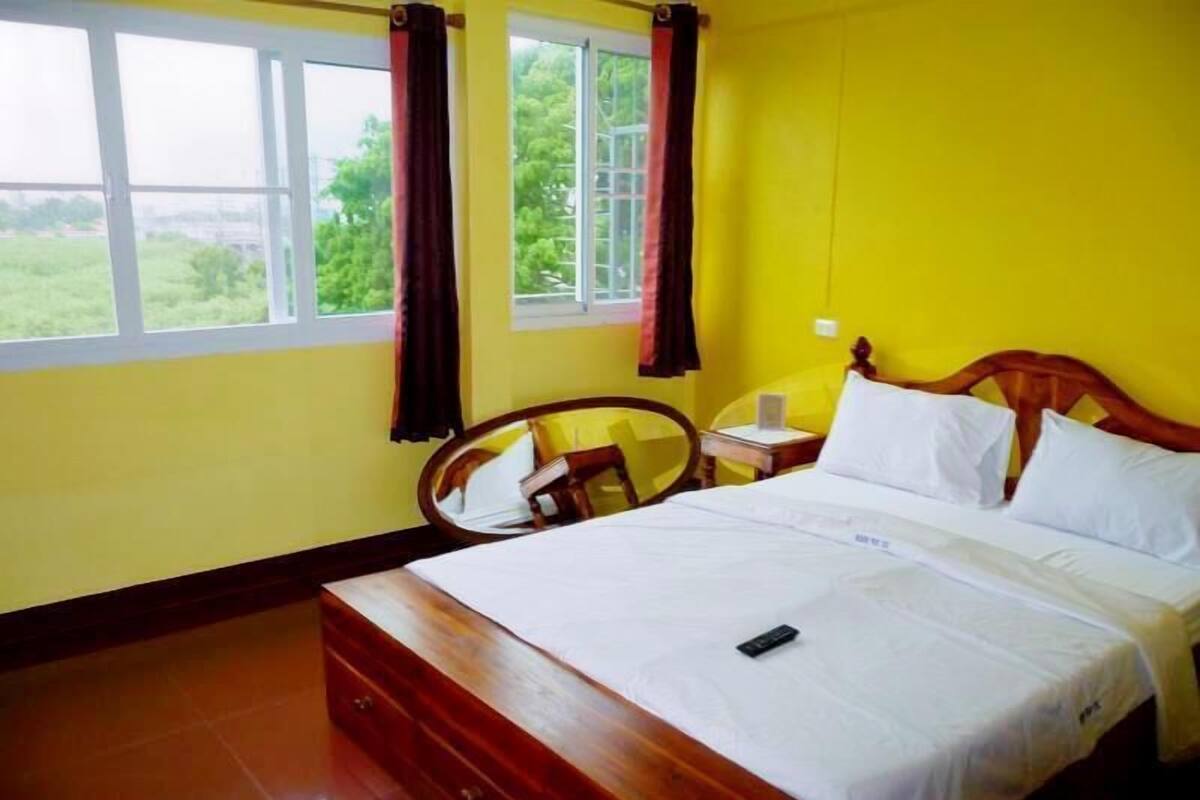 A bedroom with a bed, bedside table, chair, and a window with curtains.