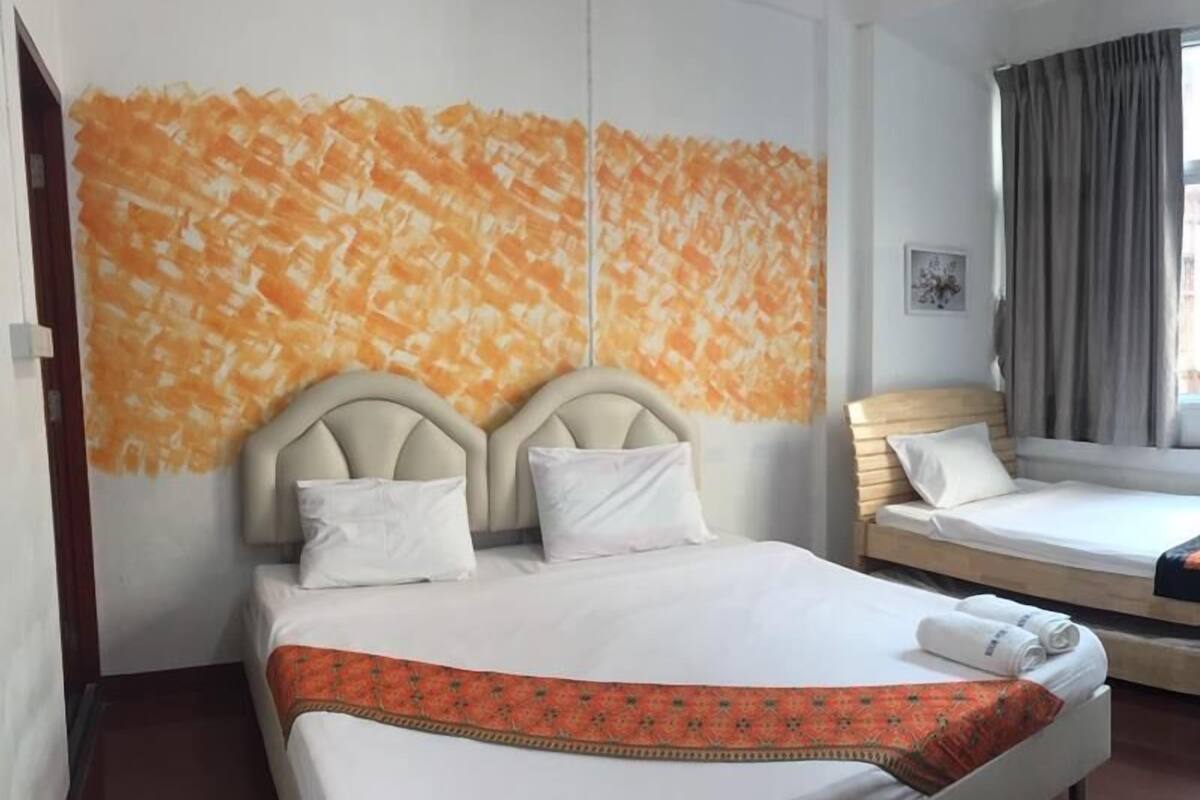 A hotel room with a large bed, a smaller bed, a window with curtains, and a wall with a patterned design.