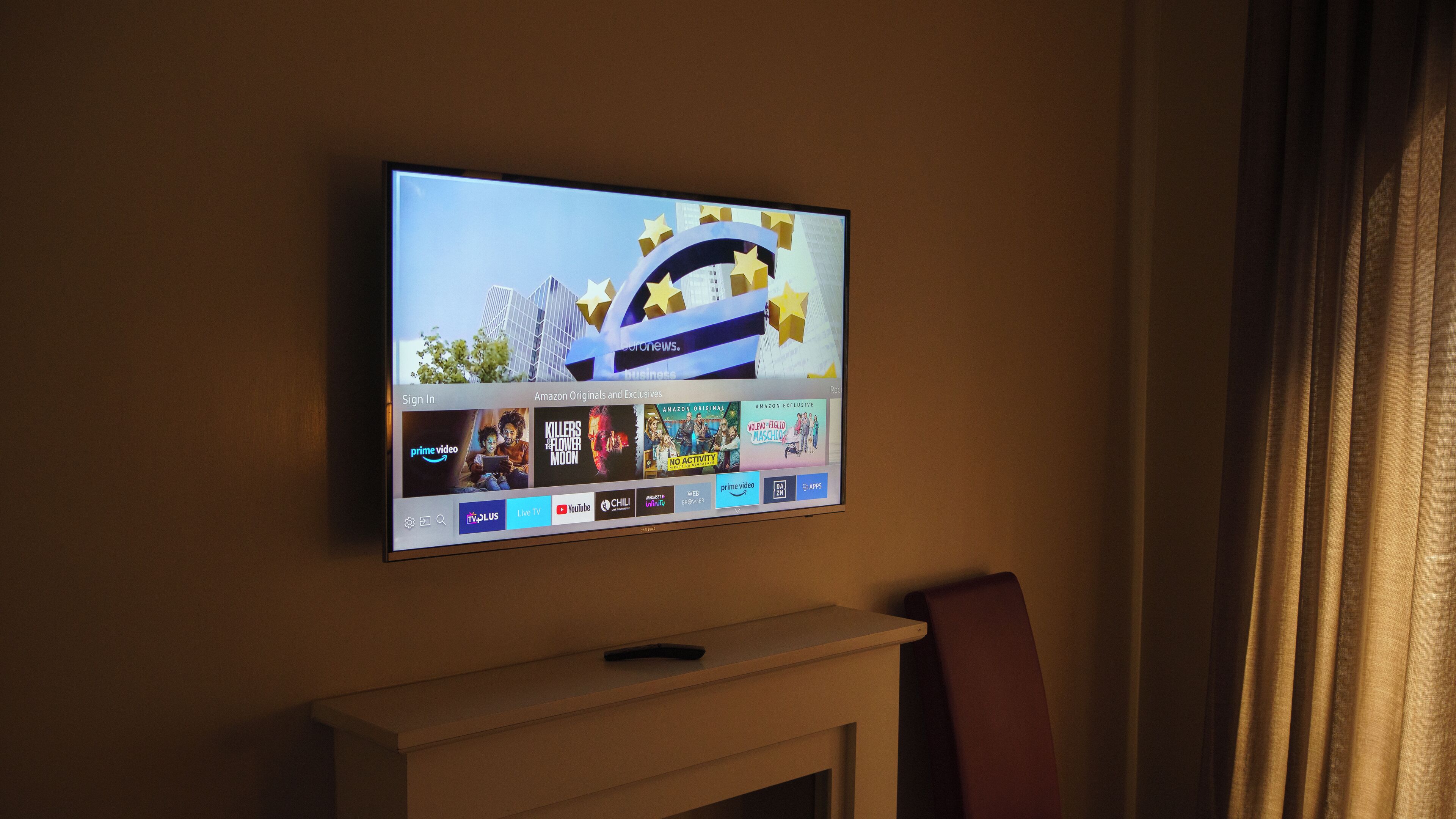 Un televisor de pantalla plana montado en la pared muestra una interfaz de servicio de transmisión con varias categorías de contenido y logotipos.