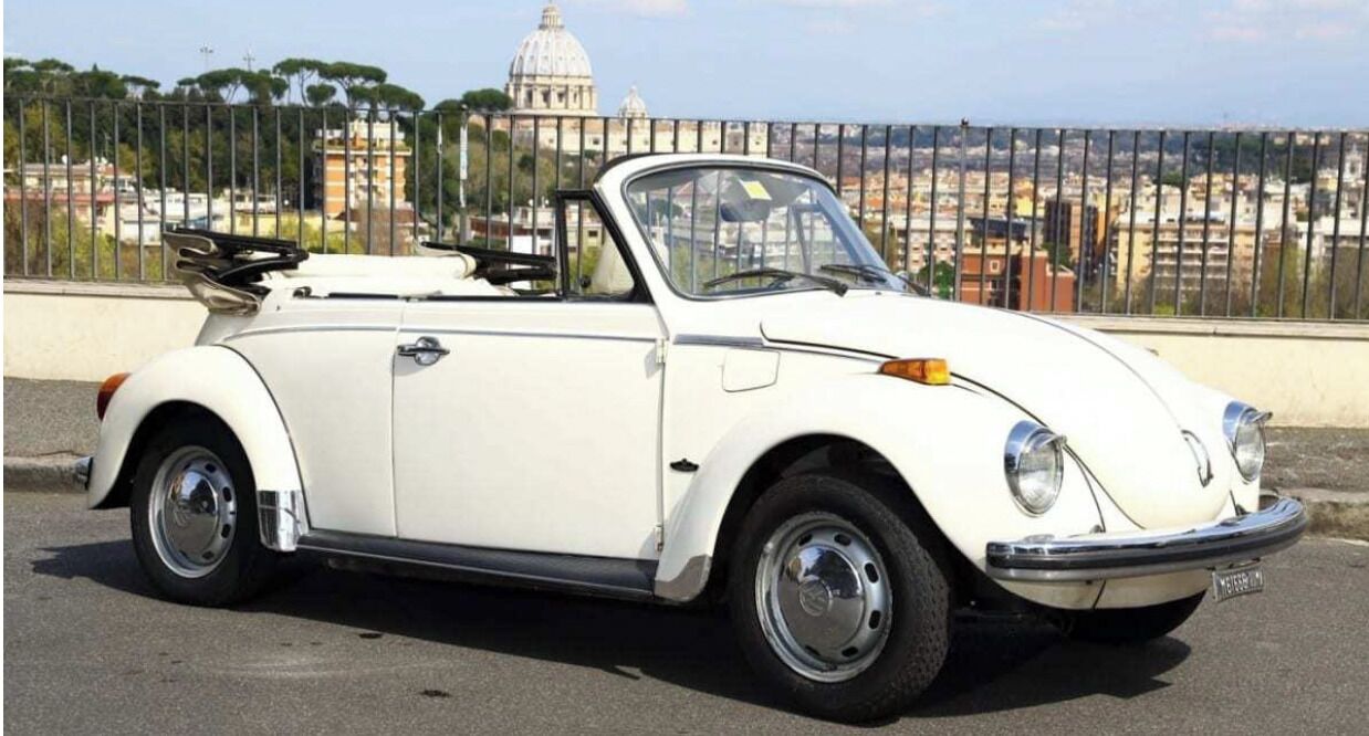 A white convertible car parked on a street with a cityscape in the background.