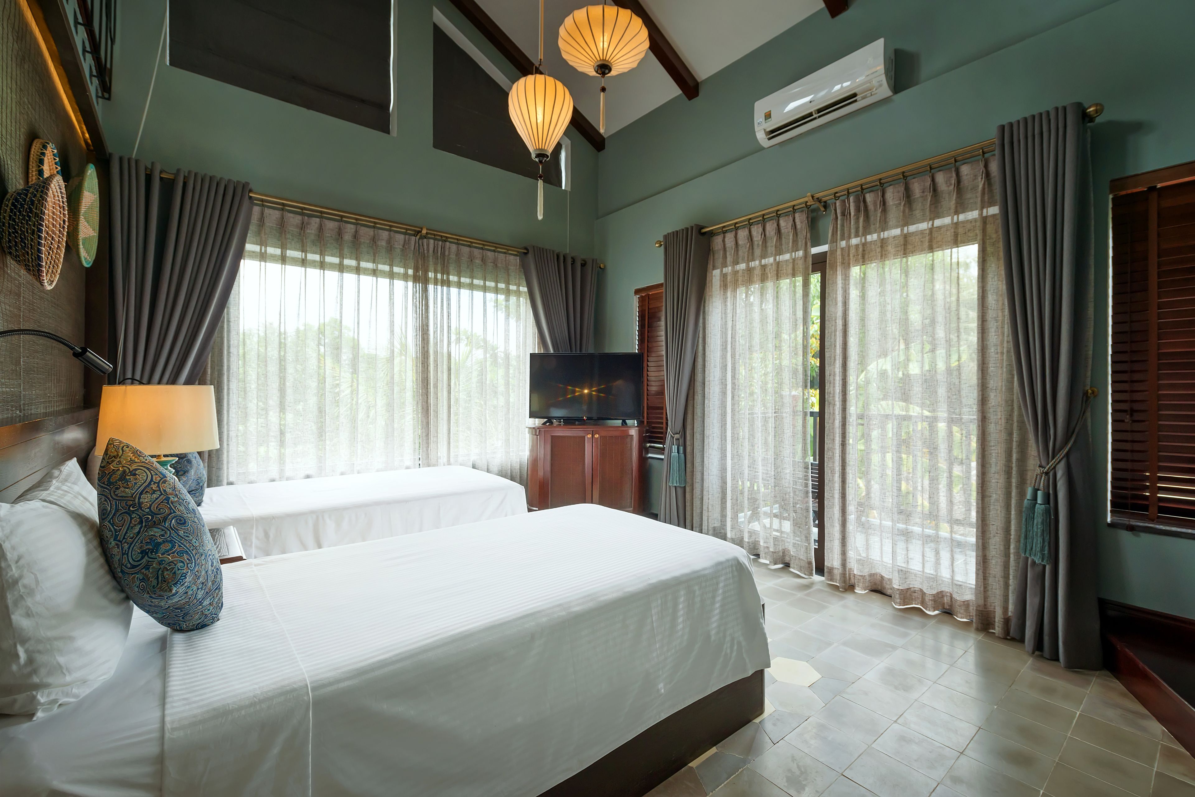 Une chambre d’hôtel avec deux lits, une télévision et de grandes fenêtres équipées de rideaux.