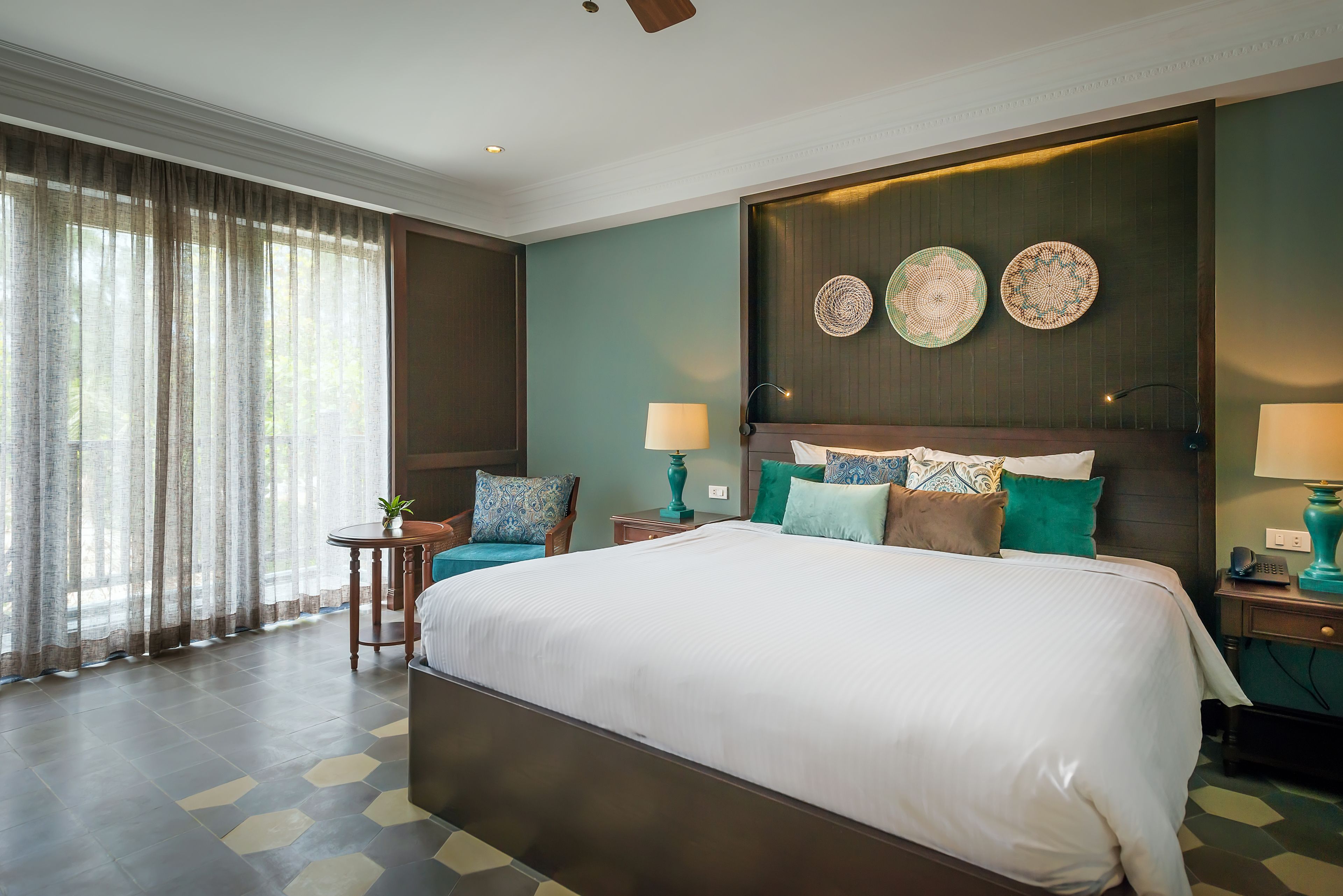 Une chambre d’hôtel avec un grand lit, une petite table avec une lampe et une vue sur l’extérieur à travers des rideaux légers.