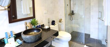 A modern bathroom with a large mirror, a vessel sink, a toilet, and a glass-enclosed shower.